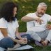 Mature couple sitting on yoga mats outdoors, sharing water and enjoying a peaceful moment.