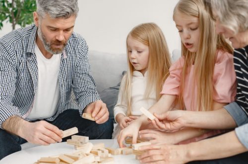 Four family members of different ages engage with toy blocks on a table indoors.