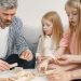 Four family members of different ages engage with toy blocks on a table indoors.