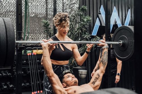 Man lifting weights with woman spotting in Mexico City gym. Urban and dynamic fitness scene.